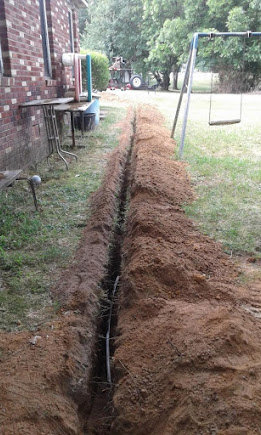 Freshly excavated sewer line trench across a Warren backyard